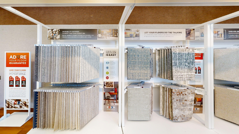 A retail display featuring hanging samples of carpet in blue, beige, white, and maroon. An 